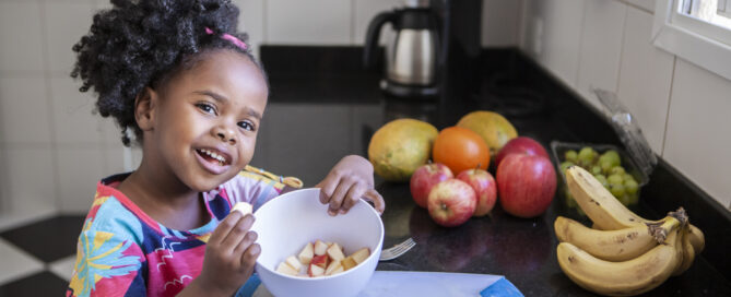 Portrait of little girl eating fruits in the kitchen with mom